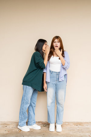 Full length shot of two young Asian woman against plain wall