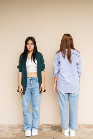 Full length shot of two young Asian woman against plain wall