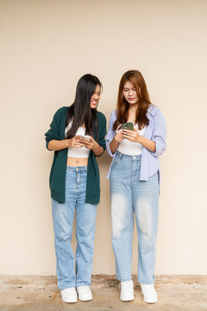 Full length shot of two young Asian woman against plain wallの写真素材