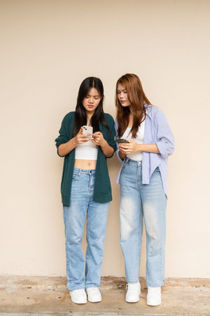 Full length shot of two young Asian woman against plain wall