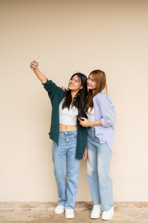 Full length shot of two young Asian woman against plain wallの写真素材