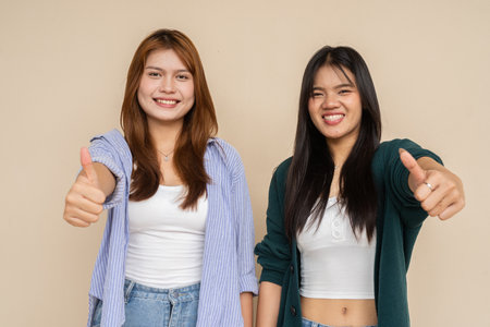 Portrait of two young Asian woman against plain wallの写真素材