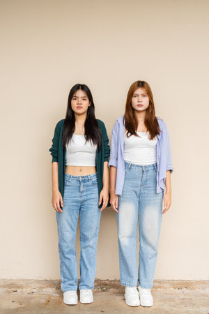 Full length shot of two young Asian woman against plain wallの写真素材