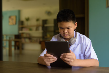 Thai Student in School Uniform Studying in Library Using Tablet Computerの写真素材