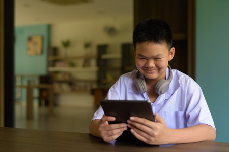 Thai Student in School Uniform Studying in Library Using Tablet Computerの写真素材