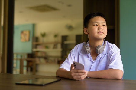 Thai Student in School Uniform Studying in Library Using Phoneの写真素材