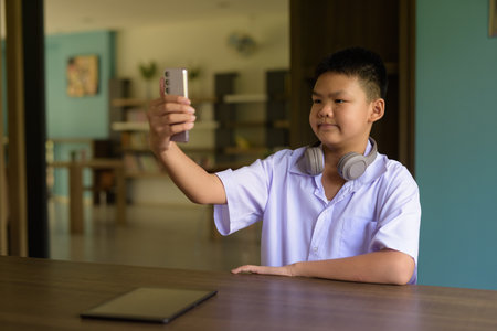 Thai Student in School Uniform Studying in Library Using Phoneの写真素材
