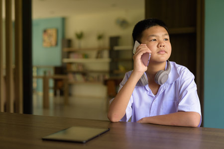 Thai Student in School Uniform Studying in Library Using Phoneの写真素材