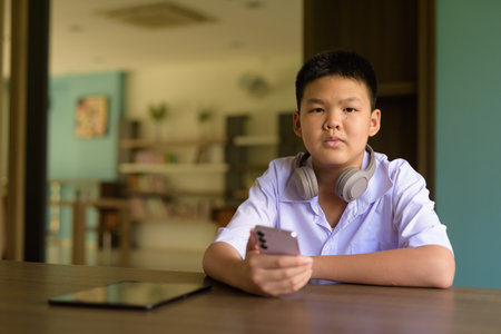 Thai Student in School Uniform Studying in Library Using Phoneの写真素材