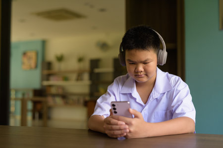 Thai Student in School Uniform Studying in Library Using Phoneの写真素材