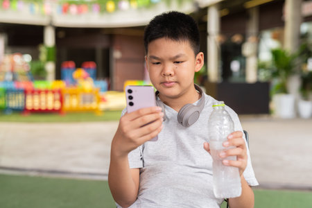 Boy drinking water and using phone while sitting outdoorsの写真素材