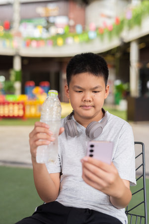 Boy drinking water and using phone while sitting outdoorsの写真素材