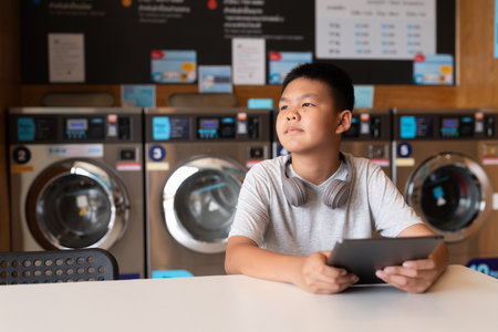 Asian teenage student boy using diigtal tablet in laundry shopの写真素材