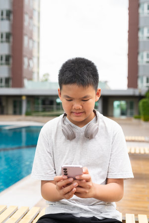 Asian Teenage Boy at Poolside During Summer Using Mobile Phone