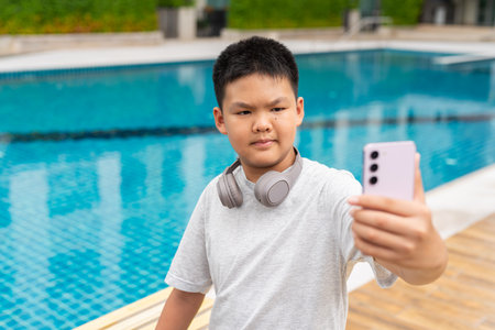 Asian Teenage Boy at Poolside During Summer Using Mobile Phoneの写真素材