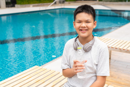 Asian Teenage Boy at Poolside During Summer Drinking Waterの写真素材