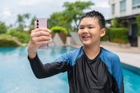 Asian teenage boy using phone after swimming in pool during summerの写真素材