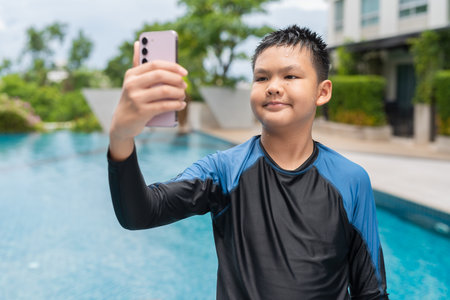 Asian teenage boy using phone after swimming in pool during summerの写真素材