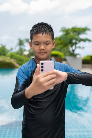 Asian teenage boy using phone after swimming in pool during summerの写真素材