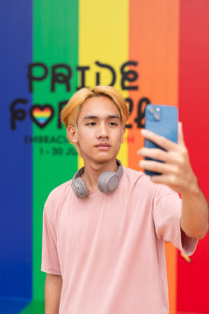Handsome gay man taking selfie with phone against pride rainbow background