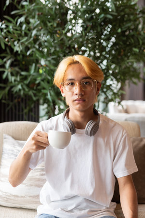 Handsome young Asian teenager man with blonde hair inside cafe restaurantの写真素材