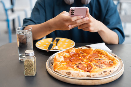Young man taking photo of pepperoni pizza in outdoor restaurant with phoneの写真素材