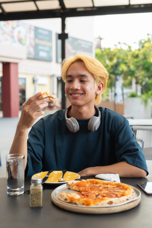 Thai gay teenager man eating pepperoni pizza in outdoor restaurant