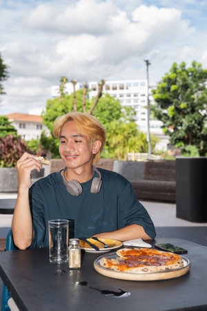Thai gay teenager man eating pepperoni pizza in outdoor restaurantの写真素材