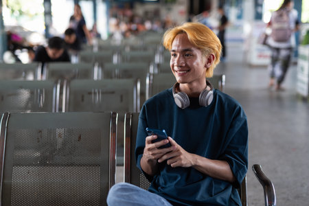 Young Asian teenage tourist man in bus station using smartphone