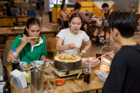 Friends eating Thai Food BBQ Grill Mu Kratha at nightの写真素材