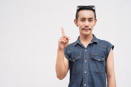 Portrait of nonbinary genderfluid young Asian gay man against white wallの写真素材