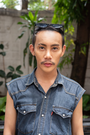 Portrait of nonbinary genderfluid young Asian gay man sitting outdoors during summer