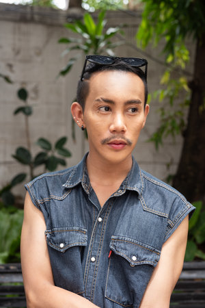 Portrait of nonbinary genderfluid young Asian gay man sitting outdoors during summerの写真素材
