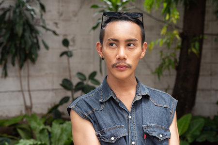 Portrait of nonbinary genderfluid young Asian gay man sitting outdoors during summerの写真素材