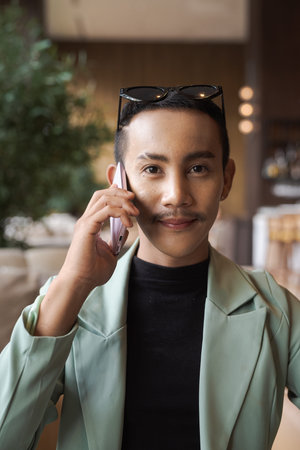 Portrait of nonbinary genderfluid young Thai gay businessman using phone in cafe