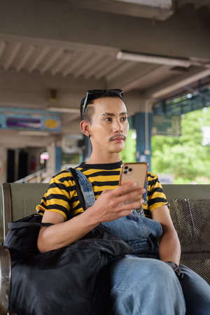 Cute nonbinary genderfluid young Asian gay tourist man in bus terminal
