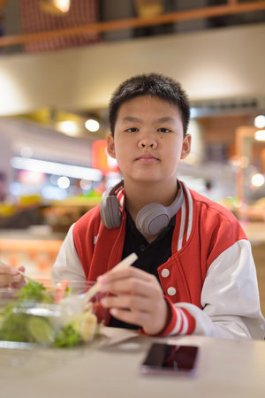 Handsome Teen Thai boy wearing headphones eating salad in cafeteria