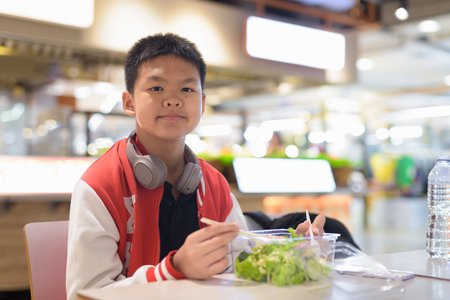 Young Thai teenage boy eating salad indoors in cafeの写真素材
