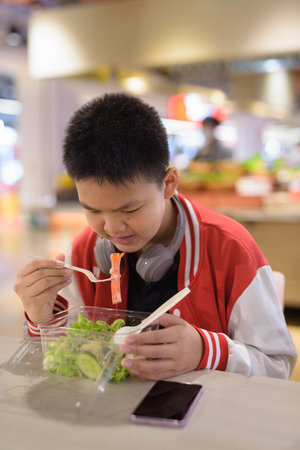 Young Thai teenage boy eating salad indoors in cafeの写真素材