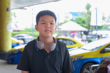 Young Thai teen boy wearing headphones with city taxis in backgroundの写真素材