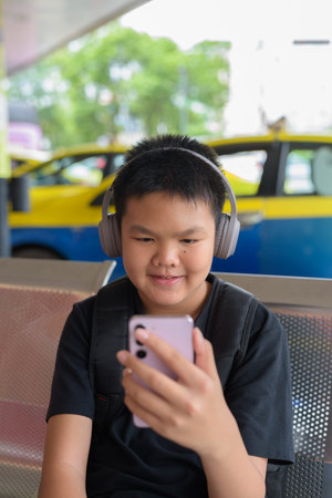 Young Thai teen boy wearing headphones using phone with city taxis in background