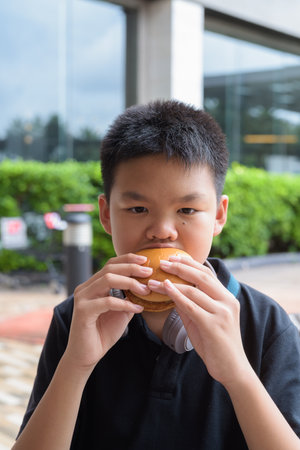Thai student boy wearing headphones eating burger at outdoor tableの写真素材