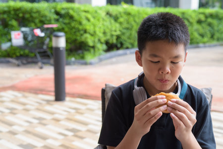 Thai student boy wearing headphones eating burger at outdoor tableの写真素材