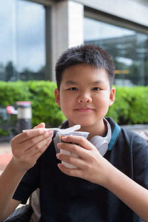 Thai boy eating vanilla soft serve ice cream with chocolate syrup outdoorsの写真素材