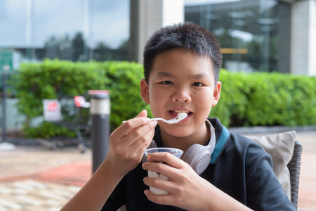 Thai boy eating vanilla soft serve ice cream with chocolate syrup outdoorsの写真素材