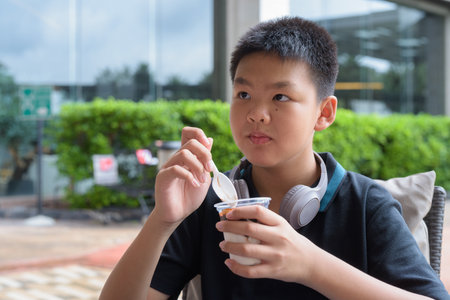 Thai boy eating vanilla soft serve ice cream with chocolate syrup outdoorsの写真素材