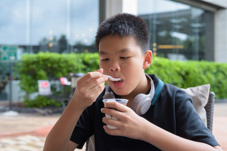 Thai boy eating vanilla soft serve ice cream with chocolate syrup outdoorsの写真素材