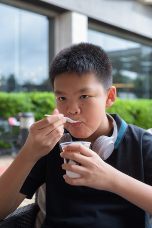 Thai boy eating vanilla soft serve ice cream with chocolate syrup outdoorsの写真素材