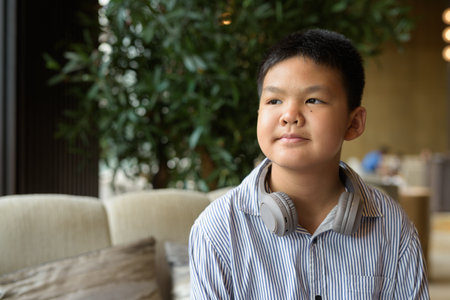 Portrait of Thai boy sitting at cafe with headphonesの写真素材