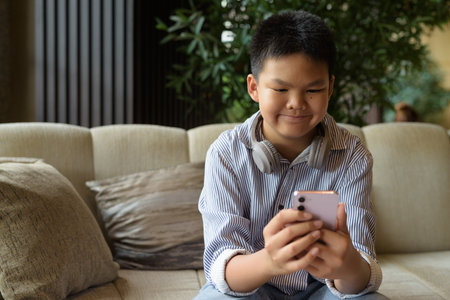 Happy Thai boy using phone at cafe with headphonesの写真素材